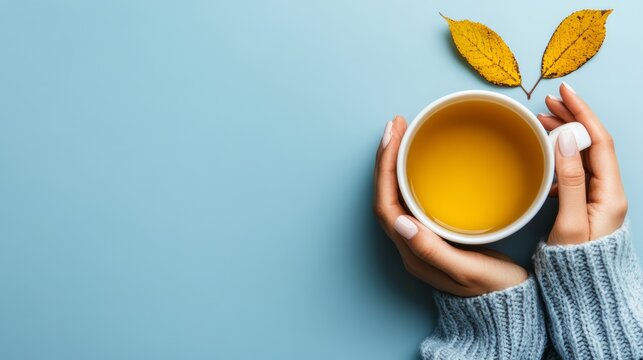 Cozy Autumn Brew: Hands wrapped in a warm, knitted sweater gently cradle a steaming mug of amber tea, adorned with delicate yellow autumn leaves, creating a serene moment of comfort.