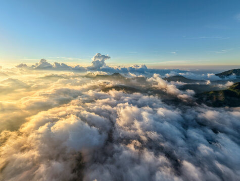 Aerial view of the sea of clouds surrounding the peaks of Gunung Bismo at sunrise with golden light illuminating the mountain ridges in Kecamatan Kejajar, Jawa Tengah, Indonesia.