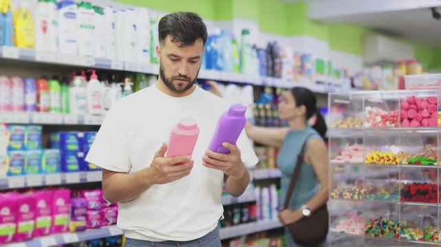 Man examines product shampoo or shower gel while purchase in store. Customer near display case looks at product, pays attention to features and manufacturer