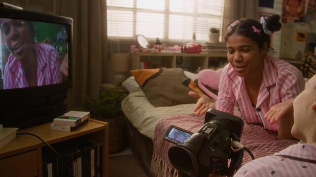 African American teenage girl and Caucasian teenager recording video blog with retro camcorder in bedroom. Footage ideal for youth culture, social media marketing, and retro technology commercials