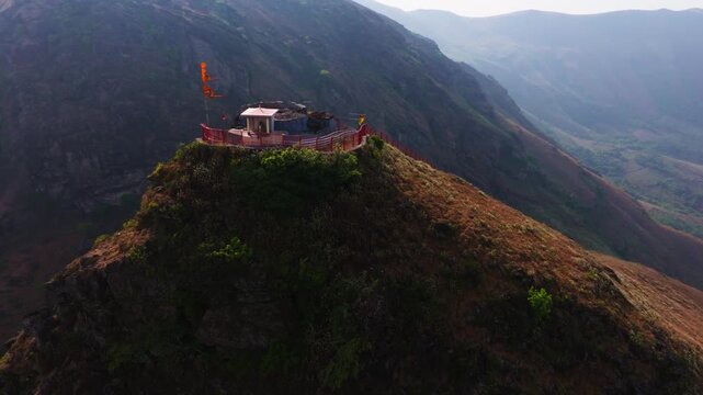 Hilltop temple with swinging religion flag, fog and round mountain at Bababudangiri, Chikkamagaluru, karnataka, india. day time, semi orbit shot, drone shot, 4k.