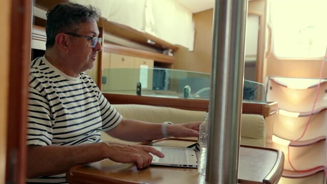 Digital nomad working on a laptop inside a sailboat cabin