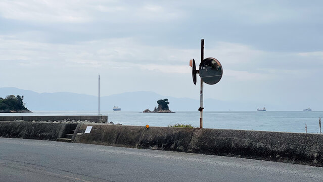 高松市の海岸沿いの道路とカーブミラー、防波堤の向こうに広がる穏やかな瀬戸内海と行き交う貨物船のノスタルジックな風景。
