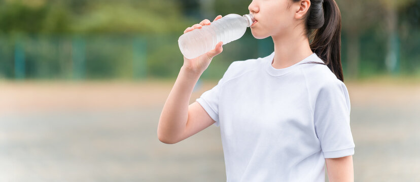 Junior high and high school girls in gym clothes drinking water during exercise.