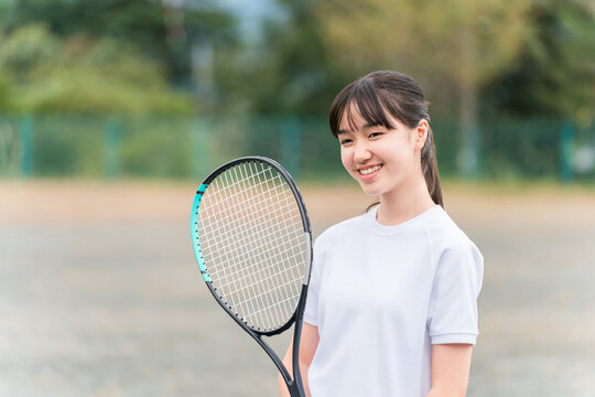 Elementary, middle, and high school girls in gym clothes playing tennis on the school grounds.