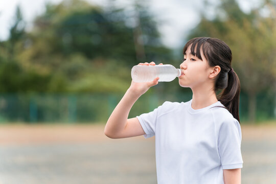 Junior high and high school girls in gym clothes drinking water during exercise.