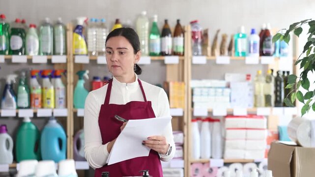Saleswoman carefully counts the balance of goods and writes down in the documents that then replenish the stock of the warehouse. Supermarket worker conducts an inventory of household chemicals 