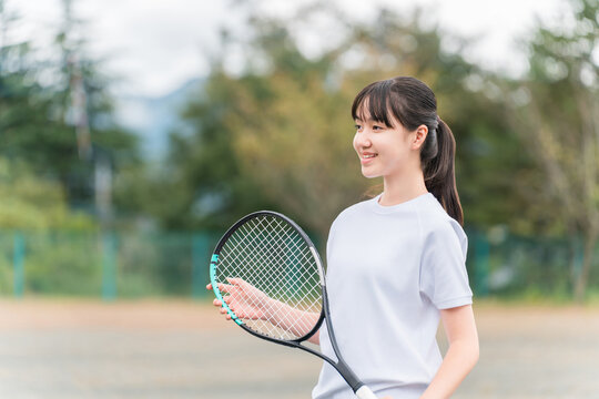 Elementary, middle, and high school girls in gym clothes playing tennis on the school grounds.
