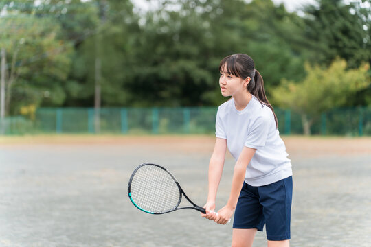 Elementary, middle, and high school girls in gym clothes playing tennis on the school grounds.