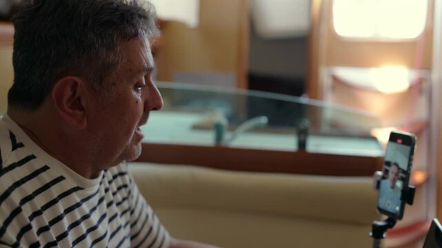Mature man vlogging and talking on smartphone camera on a yacht