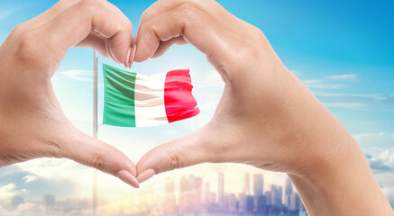 Italy national flag. Two hands forming a heart shape in front of a national flag waving in beautiful clouds. Italy national flag behind the heart shape hand.