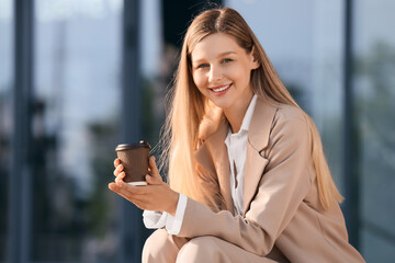 Fototapeta premium Smiling young woman holding coffee cup outdoors