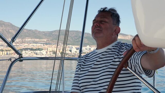 Mature sailor steering sailboat yacht at sea