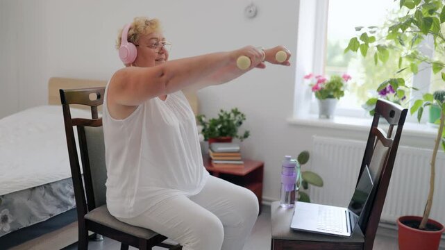 Overweight older lady doing front dumbbell raises during home workout fitness at home