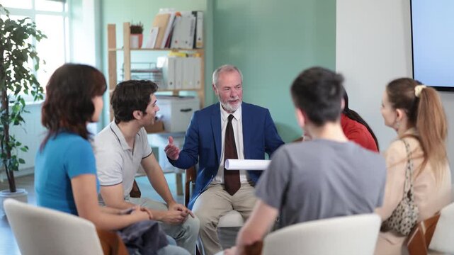 Elderly teacher gives a lecture to a group of students who are sitting in a circle. Qualified psychologist communicates with a group of young people and talks about psychological support . High