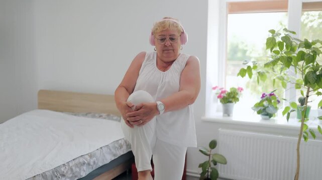 Senior woman doing standing knee chest stretch during home fitness workout fitness at home
