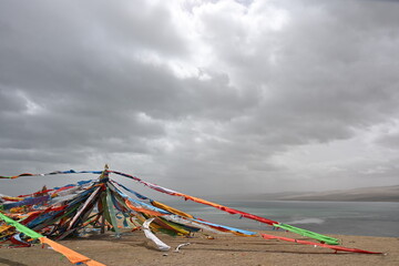 A vibrant prayer flag tower rises against the mountain sky, its layered colors whispering ancient mantras with every flutter of the Himalayan wind. © Sean Zhang