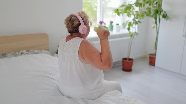 Side view of mature grandmother doing dumbbell front raises at home fitness at home