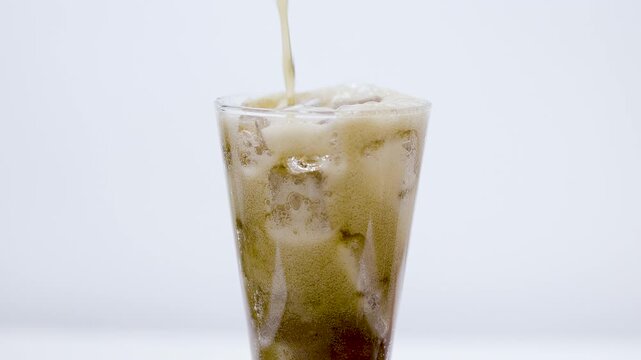 A close-up of cola splashing dynamically out of a glass filled with ice cubes against a white background.