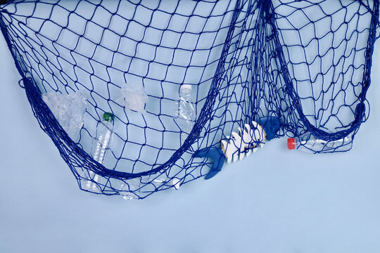Plastic waste and fish bones caught in blue fishing net on light background