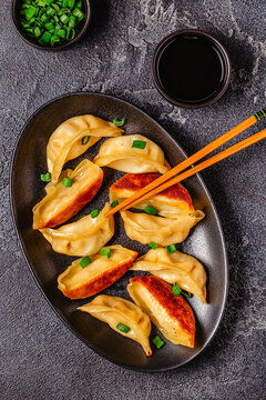 Dumplings are served on a black plate with green onion