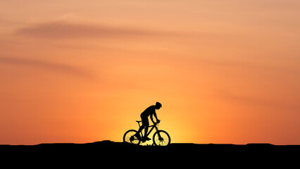 Obraz premium Silhouette of Cyclist Riding Against a Vibrant Orange Sunset on a Calm Evening