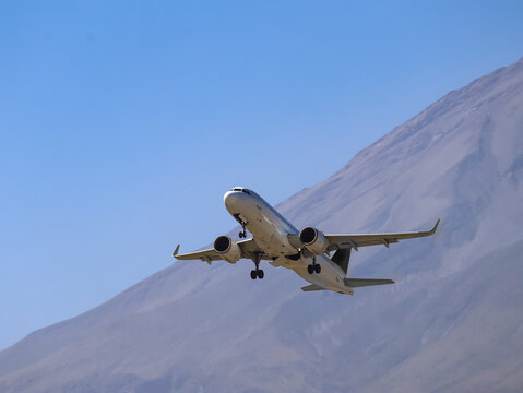 White twin-engine commercial plane approaching runway with volcano behind