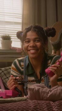 Portrait of African American female teenager smiling, holding pink retro telephone receiver and looking at camera. Footage is perfect for nostalgic youth communication ads, vertical