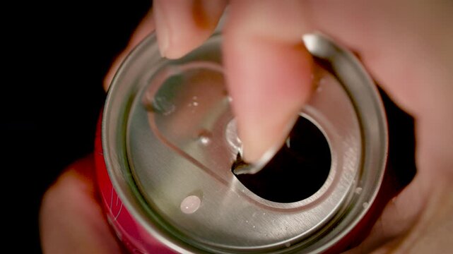  A close-up of a hand pulling the tab of a metal can to open it against a soft blurred background.