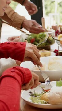 Vertical video: Serving male host in tan shirt leaning forward, spooning salad onto plates at home