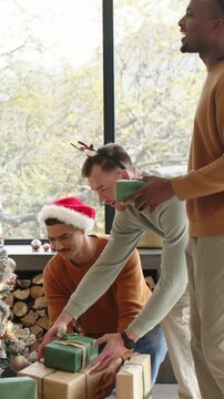 Vertical video: Kneeling man holding gifts trio arranging by Xmas tree home with Santa hat antlers