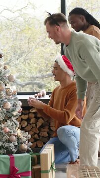 Vertical video: Decorating trio placing ornaments by window, green-top bending, stepping back