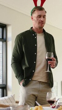 Vertical video: Shifting weight, man toasting at dining table with wine glass and red antlers