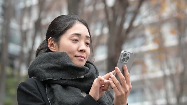 冬の屋外でスマートフォンを操作しながら微笑む30代の日本人女性