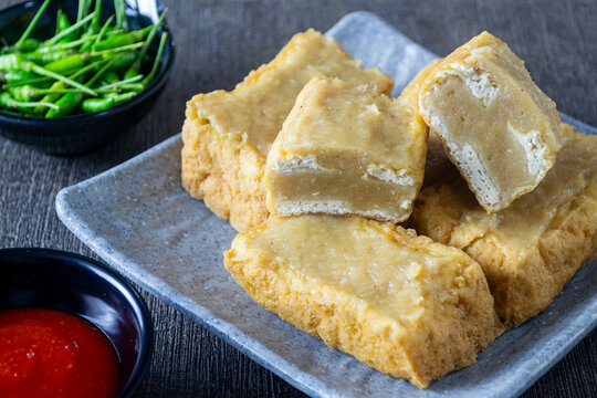 Indonesian street food Tahu Bakso, fried tofu stuffed with savory meatball filling, served with chili sauce and green chilies on a plate