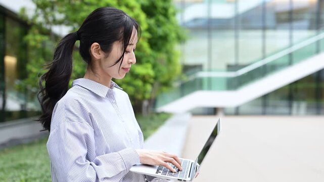 オフィス街でノートパソコンを使って仕事をする30代の日本人ビジネスパーソンの女性