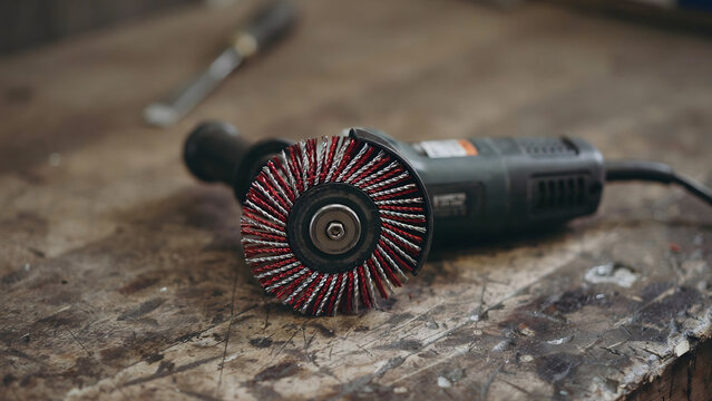Angle grinder with a wire brush wheel resting on a wooden workshop workbench