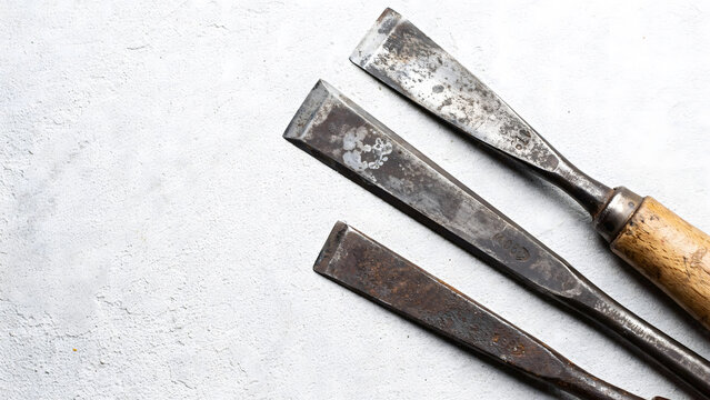 Three old rusted wood chisels arranged diagonally on a textured white surface