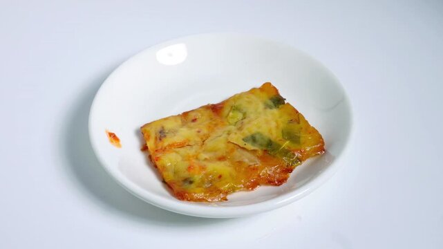 Hand grab a piece of pajeon korean pancake snack with fork and take a bite of it outside the frame isolated on horizontal white background.