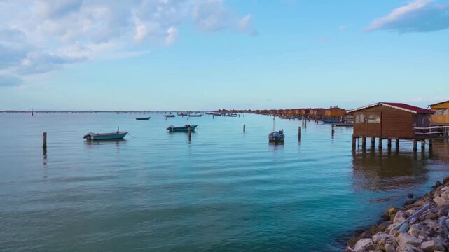 Traditional wooden stilt houses and small fishing boats are anchored in a calm sea lagoon