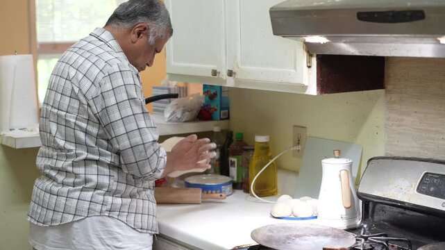 Older Pakistani man flipping roti dough on counter