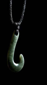 A slender green jade pendant shaped like a silique on a dark background.
