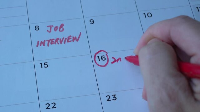Writing down second interview appointment on table calendar with red marker. Close up view. Employment or careers concept.
