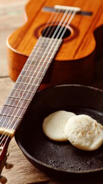 Arepas on cast-iron griddle beside cuatro guitar, tropical culinary and music scene.
