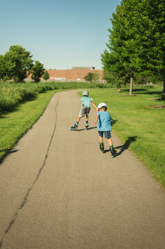 Backview of two boys rollerblading on a sunny park path