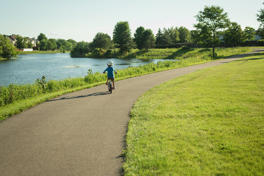 Backview of young boy riding bike on path next to lake