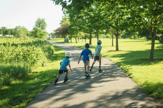 Three young boys rollerblading on a park trail