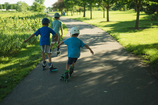Three boys rollerblading together on a sunny park path