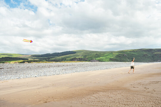 Man flying a colorful kite on a wide sandy beac