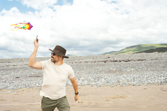 Smiling man flying a colorful kite on the beach